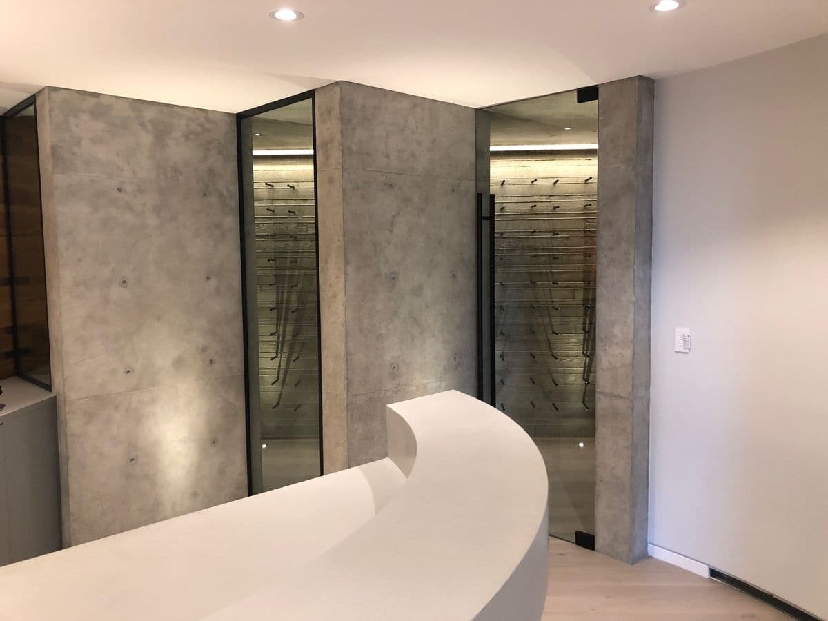 Polished board-formed concrete feature walls with glass-enclosed wine display niches in a modern interior by MZ Solution