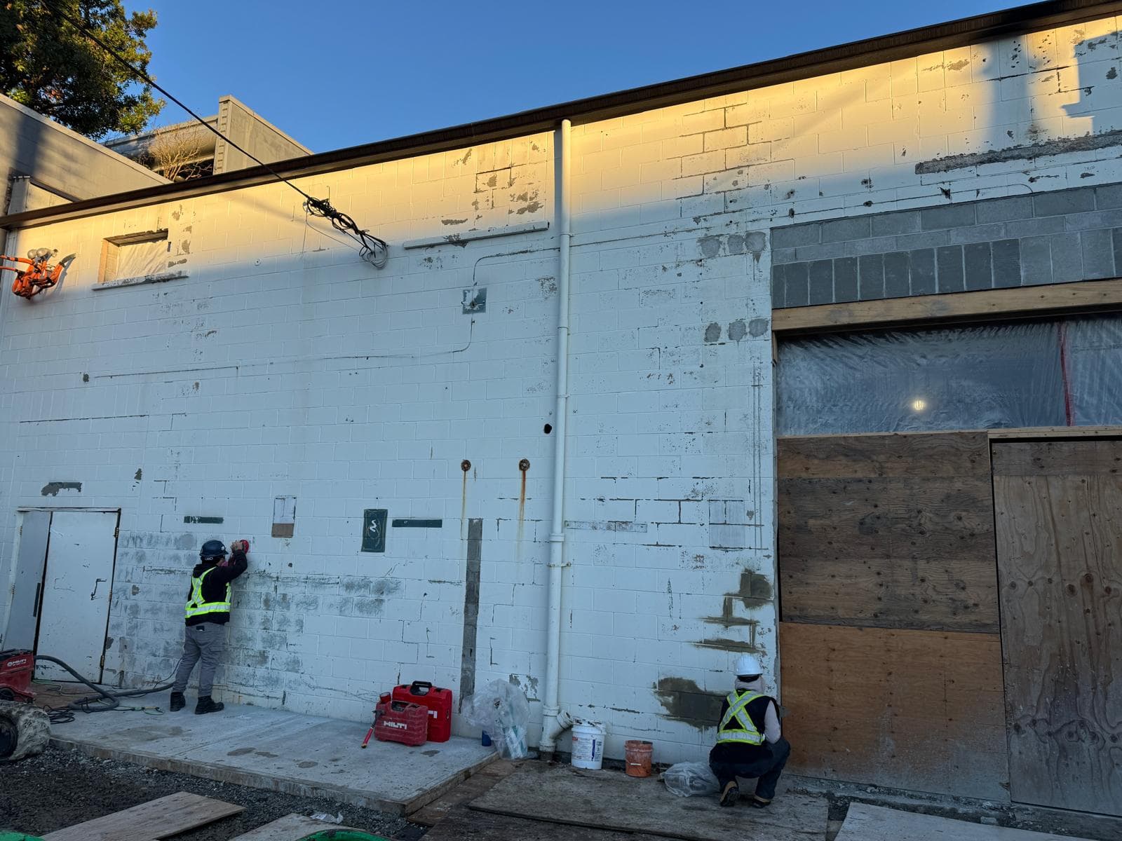 Crew grinding a stained, peeling painted exterior wall before restoration