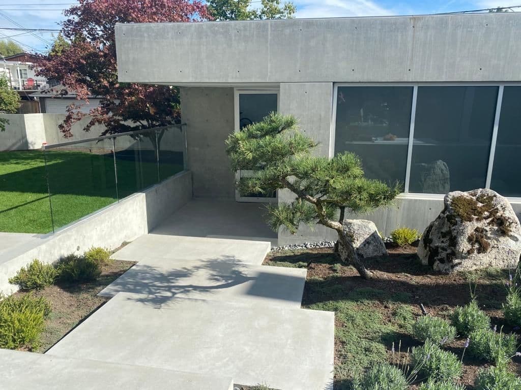 Modern concrete home with a polished patio, glass railing, and landscaped courtyard built by MZ Solution